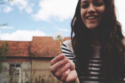 Close-up portrait of woman holding dandelion against sky