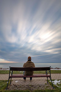 Rear view of man sitting on bench against sky