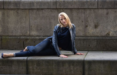 Portrait of young woman sitting against wall