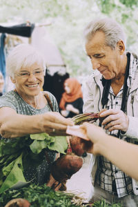 Senior woman paying to vendor while shopping for vegetables at market in city