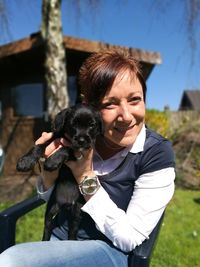 Portrait of smiling woman holding puppy while sitting on chair