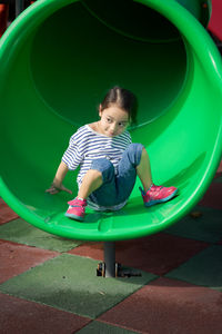 Little girl playing at the playground. sitting at the end of the slide.