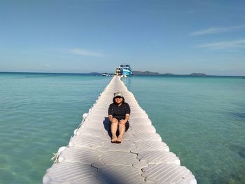 Woman sitting on pier amidst sea against sky