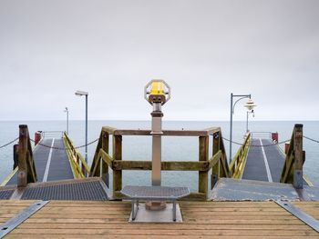 Street lights on pier by sea against sky