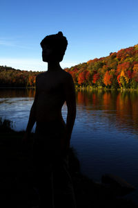 Man standing by lake against sky during sunset