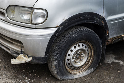 Gray car is old, with a punctured wheel and a damaged fog headlight.