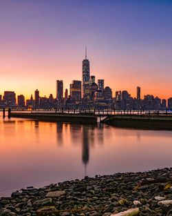 Sea by buildings against sky during sunset