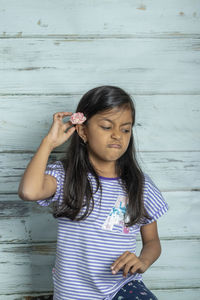 Girl looking away while sitting against wooden wall