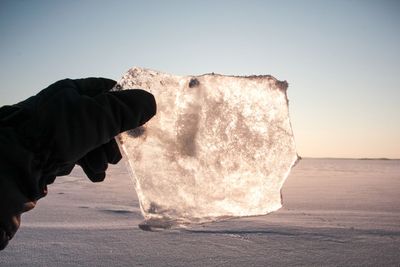 Cropped image of hand holding ice against snow covered field during winter