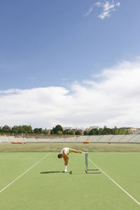 Athlete doing stretching exercise at sports field on sunny day