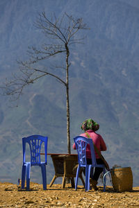 Rear view of woman sitting on chair against mountain