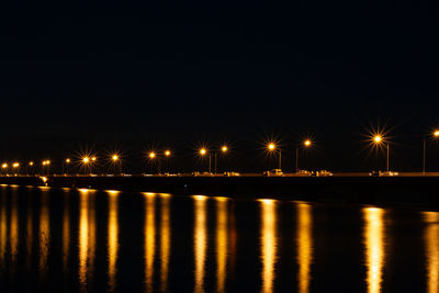Illuminated street lights by river against sky at night