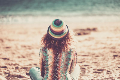 Rear view of woman sitting on beach against sky