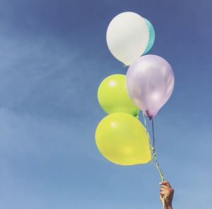 Cropped hand of person holding balloons against sky