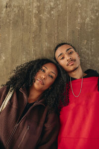 Portrait of multiracial male and female friends leaning on each other against wall