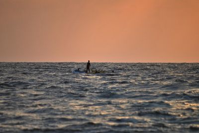 Distant view of man riding on jet boat amidst sea against clear sky during sunset