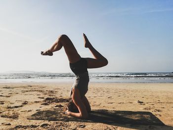 Full length of woman headstand on beach against sky