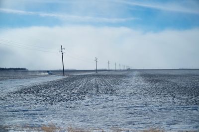 Electricity pylons on snow covered field against cloudy sky