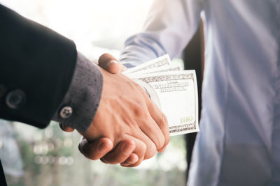 Close-up of human hand giving money to businessman while shaking hands in office