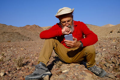 Senior man using mobile phone sitting on rock