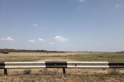 Empty bench on field against sky