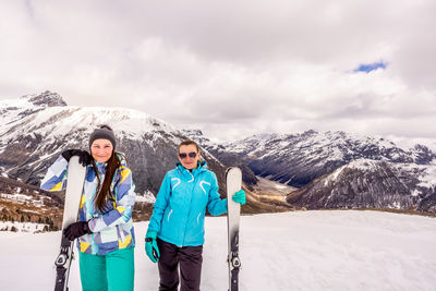 Portrait of smiling friends with snowboards standing on snowcapped mountain against sky