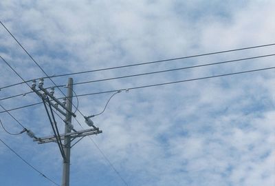 Low angle view of electricity pylon against cloudy sky