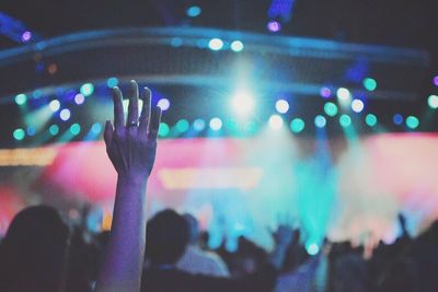 Cropped hand raised against illuminated lights at concert