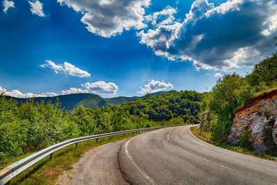 Empty road amidst trees against sky