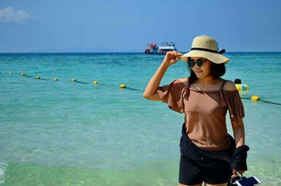 Woman wearing sunglasses standing at beach on sunny day