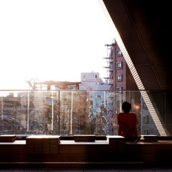 Rear view of man sitting by glass railing