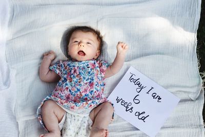 High angle view of cute baby girl with text lying on bed at home