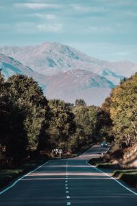 Road amidst trees and mountains against sky