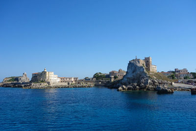 Buildings by sea against clear blue sky