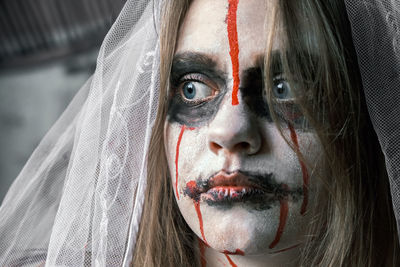 Close-up portrait of zombie woman in wedding dress with veil and stage makeup looking side. 