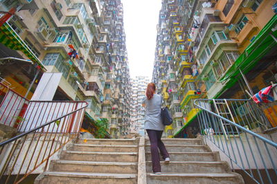 Rear view of woman on staircase amidst buildings in city
