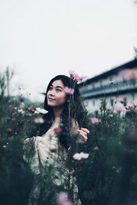 Smiling young woman standing by flower tree against sky