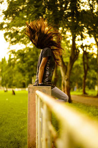 Side view of woman tossing hair while sitting on railing