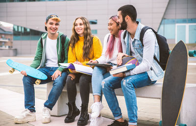 Full length of smiling friends sitting on bench outdoors