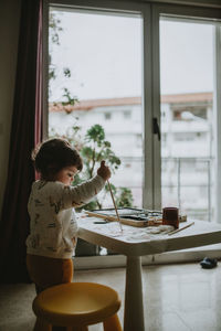 Side view of girl painting over paper on table at home
