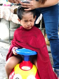 Midsection of woman cutting boy hair sitting on toy car