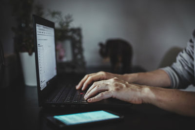 A woman works remotely from her home with a laptop and her phone.