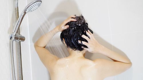 Rear view of shirtless woman bathing in bathroom