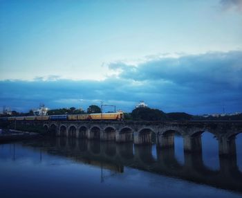 Arch bridge over river against sky at dusk