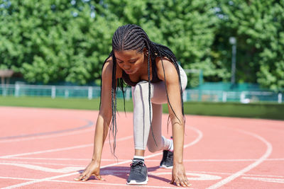 African american woman with long braids prepares low start running action on red track at stadium