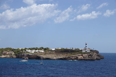 Lighthouse amidst sea and buildings against sky