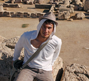 Portrait of young man wearing hat while sitting on rock