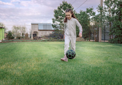 Cute little girl playing football with soccer ball on green lawn in backyard of house. child kicking 