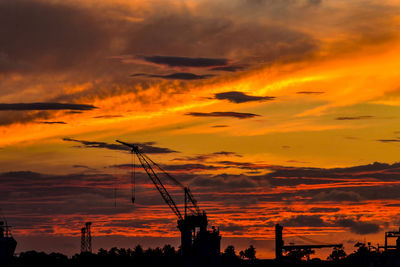 Silhouette of cranes against dramatic sky during sunset