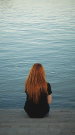 Rear view of woman sitting by lake